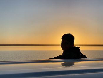 Silhouette man by sea against sky during sunset