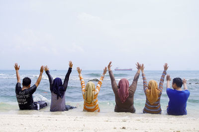 Rear view of people at beach against sky