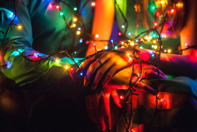 Midsection of couple with colorful illuminated string lights