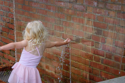 Rear view of girl touching artificial waterfall over brick wall