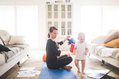 Side view of mid adult female parent looking at daughter while exercising in home office