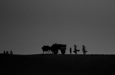 Silhouette people riding horse on field against sky