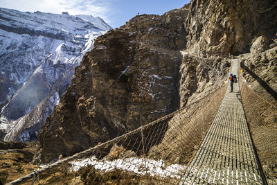 Side view of unrecognizable backpacker standing on metal suspension bridge and admiring view of rocky himalayas mountains on sunny day in nepal