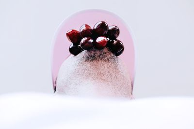 Close-up of young man with fruit in mouth against white background
