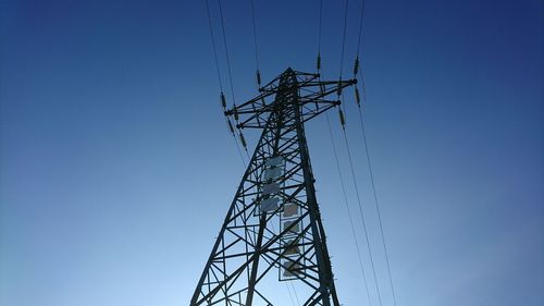 Low angle view of electricity pylon against clear blue sky