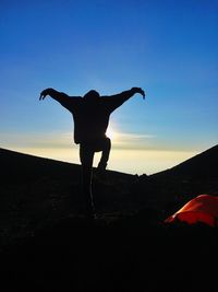 Silhouette man with arms raised against clear sky