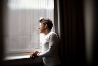 Young man standing by glass window at home