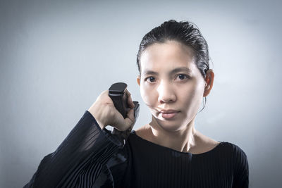 Portrait of young woman holding camera against gray background