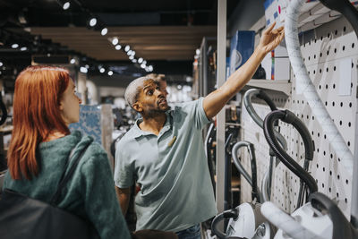 Salesman advising female customer in buying modern appliance at electronics store