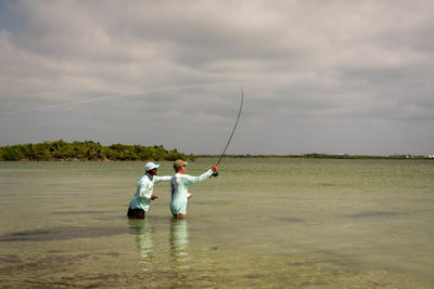 Men fishing in sea against sky