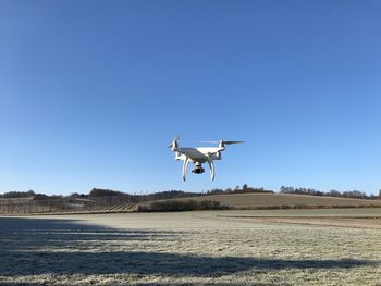 Airplane flying over field against clear blue sky