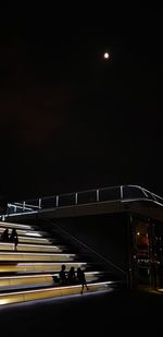 People on illuminated street against sky at night