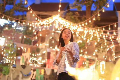 Young woman standing against illuminated lights at night