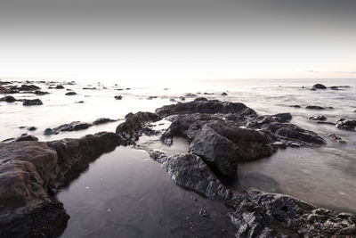 Rocks on beach against clear sky in black and white