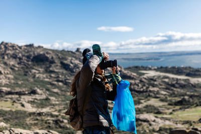 Low angle view of man photographing against blue sky