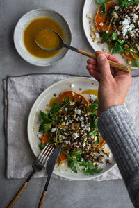 From above unrecognizable person taking spoon of sauce for scrumptious salad while preparing lunch on gray table