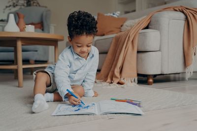 Cute boy drawing in book at home