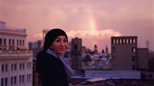 Portrait of young woman standing against cityscape during sunset