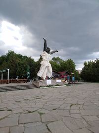Statue of people on footpath against cloudy sky