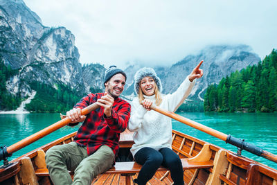 Young couple sitting on boat in sea against mountain