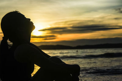 Silhouette man sitting by sea against sky during sunset