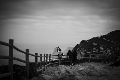 People standing on railing by sea against sky