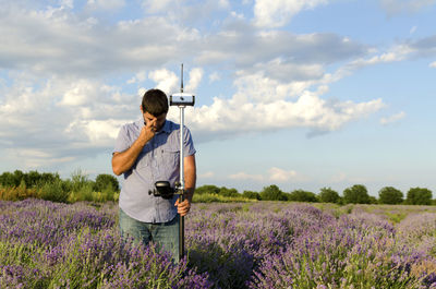 Surveyor with theodolite on lavender field against sky