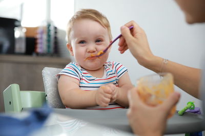 Cropped hand of parent feeding toddler son at home