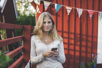 Portrait of teenage girl using mobile phone against house in back yard