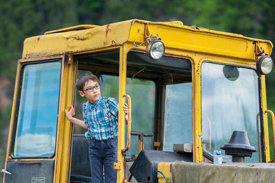 Boy looking away while standing in construction vehicle
