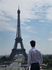 Rear view of man standing against eiffel tower and sky in city