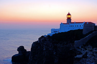 Lighthouse by sea against sky during sunset