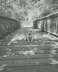Portrait of cute baby girl kneeling on footbridge at park