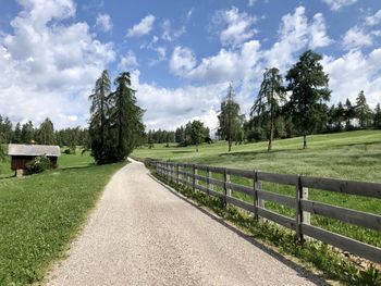 Empty road amidst trees on field against sky
