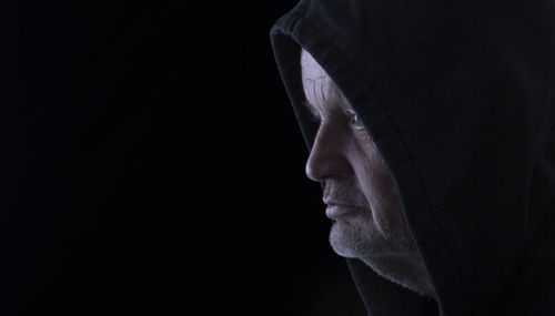 Close-up of man wearing hood against black background