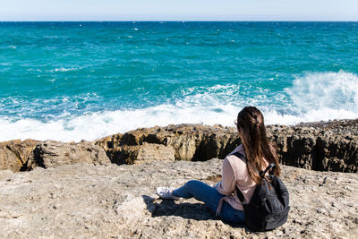 Woman sitting on shore at beach against sky