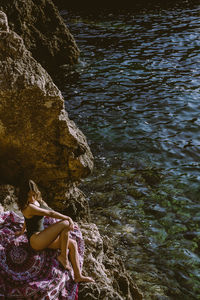 Side view of woman sitting on rock in sea