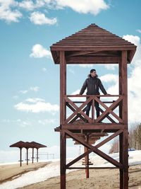 Man sitting on bench by beach against sky