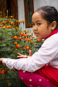 Side view of cute girl looking at red flowering plants