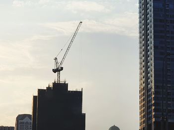 Low angle view of crane and buildings against sky