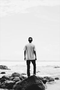 Rear view of man standing on rock at beach against sky