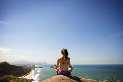 Woman meditating while sitting on rock by sea