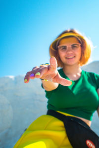 Portrait of smiling woman holding sunglasses against blue sky