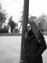 Young man with long hair wearing over coat while standing by pillar