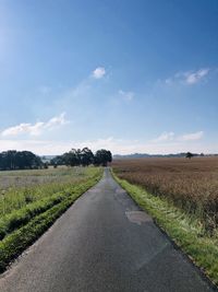 Empty road amidst field against sky