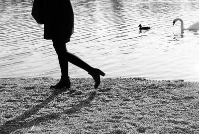 Low section of woman walking at lakeshore against birds