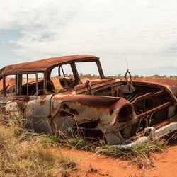 Abandoned car on field against sky