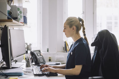 Side view of female nurse working on computer while sitting at desk in clinic