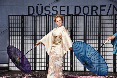 Portrait of woman with umbrella standing against the wall