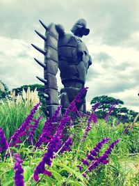 Statue of flowering plants on field against sky